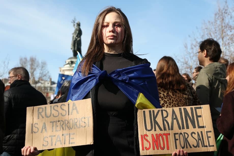Una mujer sostiene unas pancartas que dicen “Ucrania no está a la venta” y “Rusia es un Estado terrorista” durante una manifestación en París, la víspera del tercer aniversario de la invasión a gran escala.